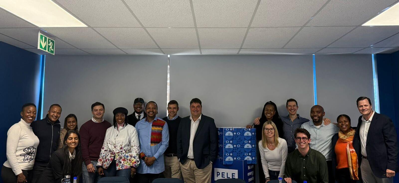 Group Photo Of All Participants Standing Together After The Signing, Smiling In Front Of A Pele Backdrop.