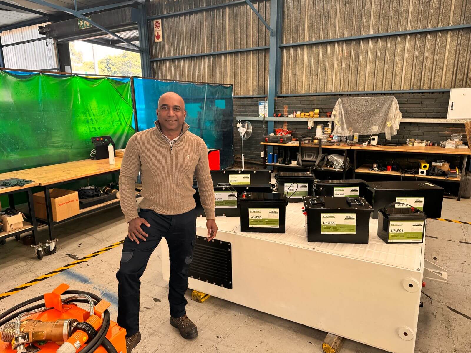 Man Standing In A Workshop Next To Equipment With An Orange Component.